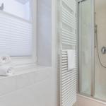 Bathroom with shower, heater, and window with blinds.