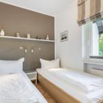 Two single beds with white bedding, wall shelf with figures, and window with view of trees.