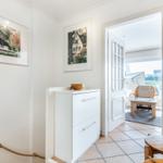 Entrance with white walls, pictures, and a white cabinet. Through door, living area with chair is visible.