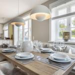 Esszimmer mit Holztisch, weißen Tischsets und Fenstern mit Blick auf Grün.