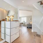 Helle Eingangshalle mit Holztreppe und weißen Schränken. Durchgang zum Wohnzimmer.