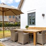 Terrasse mit Tisch, Stühlen und Sonnenschirm vor weißem Haus