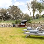 Garten mit Liegestühlen, Steinschutz und Sitzgelegenheit im Hintergrund.