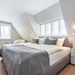 Schlafzimmer mit Dachschrägen, Bett, Nachttisch und Fenster mit Jalousien.