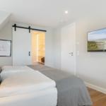 Schlafzimmer mit Dachschräge, Bett, Kleiderschrank und Wandfernseher.