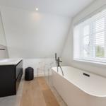 Badezimmer mit freistehender Badewanne, Waschtisch und Fenster mit Jalousie.
