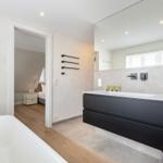 Badezimmer mit Dusche, Waschbecken und Badewanne. Blick in Schlafzimmer mit Bett.
