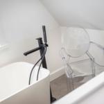 Dusche mit schwarzer Armatur und transparentem Stuhl neben Badewanne.
