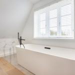 Wohnraum mit freistehender Badewanne, transparentem Stuhl und Fenster mit Jalousie.