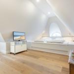 Schlafzimmer mit Dachschrägen, Bett, Fernseher und Holzboden.