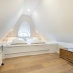 Schlafzimmer mit Doppelbett, TV und Holzfußboden unter schrägen Wänden.