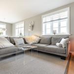 Großer Wohnbereich mit grauem Sofa, Glas-Tisch und Fenstern.