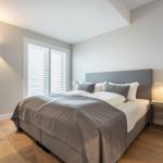 Schlafzimmer mit Bett, Nachttisch und Fenster mit Jalousie.
