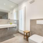 Badezimmer mit Waschbecken, Spiegel, Toilette und Holzstuhl.