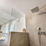 Moderne Dusche mit Regenduschkopf und Handbrause. Spiegel und Waschbecken sind sichtbar.
