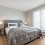 Schlafzimmer mit Bett, zwei Nachttischen und Fenster mit Jalousie.