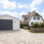 Haus mit Strohdach, weißer Garage und Kiesweg unter blauem Himmel.