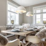 Esszimmer mit Holztisch, weißen Lampen und Fenstern mit Jalousien.