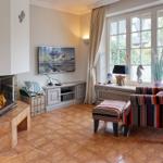 Wohnzimmer mit Kamin, Fernseher und Sessel vor Fenster.