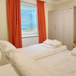 Schlafzimmer mit Bett, Kleiderschrank und Fenster mit Blick auf Strand.