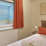 Schlafzimmer mit Bett, Nachttisch und Fenster mit Strandbild.