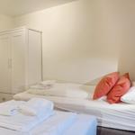 Zimmer mit zwei Betten, weißem Kleiderschrank und orangefarbenen Kissen.