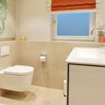 Badezimmer mit Toilette, Waschbecken und Fenster mit orangefarbenem Rollladen.