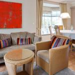 Wohnzimmer mit Sofa, Sessel und Esstisch. Große Fenster und rotes Wandbild.