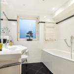 Bathroom with bathtub, sink, and bonsai plant by the window.