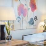 TV on wooden console with lamps and floral arrangement on wall.
