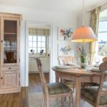 Dining room with wooden table, chairs, and glass cabinet. View of kitchen and thatched roofs.