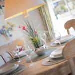 Set dining table with chairs, placemats, glasses, and flower vase.