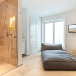 Shower area with glass enclosure, bed, and window in bedroom