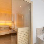 Sauna with wooden bench and bathtub with mosaic tiles