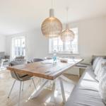 Dining area with wooden table, bench, and pendant lamps. Living area with sofa and wall art.