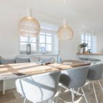Dining area with wooden table, gray chairs, and bench. Two pendant lights and windows with view.