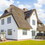 House with thatched roof and white facade. Garden area with sun lounger.