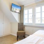 Bedroom with sloped ceiling, bed, chair, and TV.