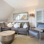 Living room with gray sofa, leather armchair, and wooden table under sloped ceiling.