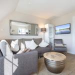 Living room with sofa, armchair, and round table. Mirror and TV on the wall.