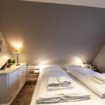 Two beds with white linens and towels in an attic room with lamps and pictures.