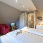 Bedroom with double bed, red armchair, and wardrobe. Door leads to bathroom.