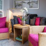 Living room with rattan furniture and pink cushions. Wall art shows dunes.
