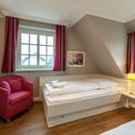 Bedroom with sloped ceiling, two windows, and a red armchair.