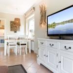 Living room with TV, dining table, and kitchen area in background.