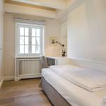 Schlafzimmer mit Bett, Schreibtisch und Fenster. Holzboden und weiße Wände.