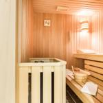 Sauna mit Holzbank, Holzwanne und Thermometer an der Wand.