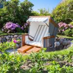 Strandkörbe mit Streifenbezug stehen im Garten mit Blumen und Steinmauer.