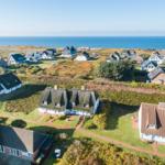 Aerielansicht von Häusern am Meer mit Grünflächen und Wegen.