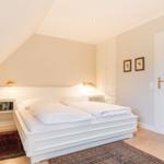 Schlafzimmer mit Doppelbett, Bücherregal und Tür.